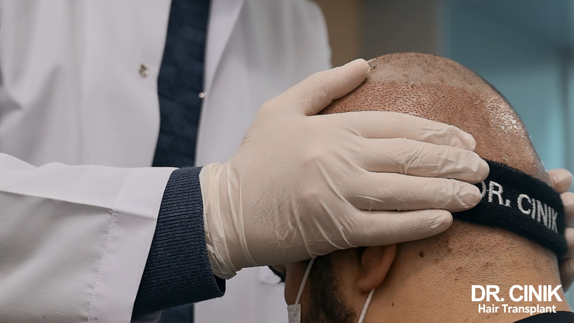 Gloved hand of a practitioner examining the head of a patient wearing a black forehead band marked Dr Cinik