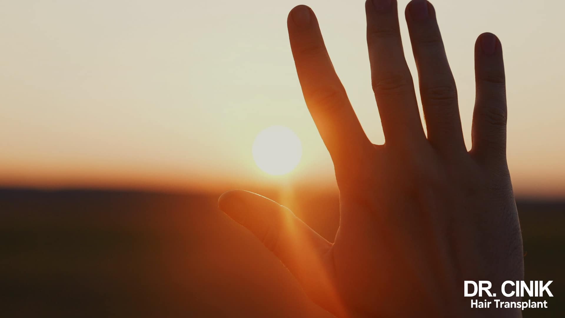 A raised hand silhouetted against a low sun sitting on the horizon, under an orange sky