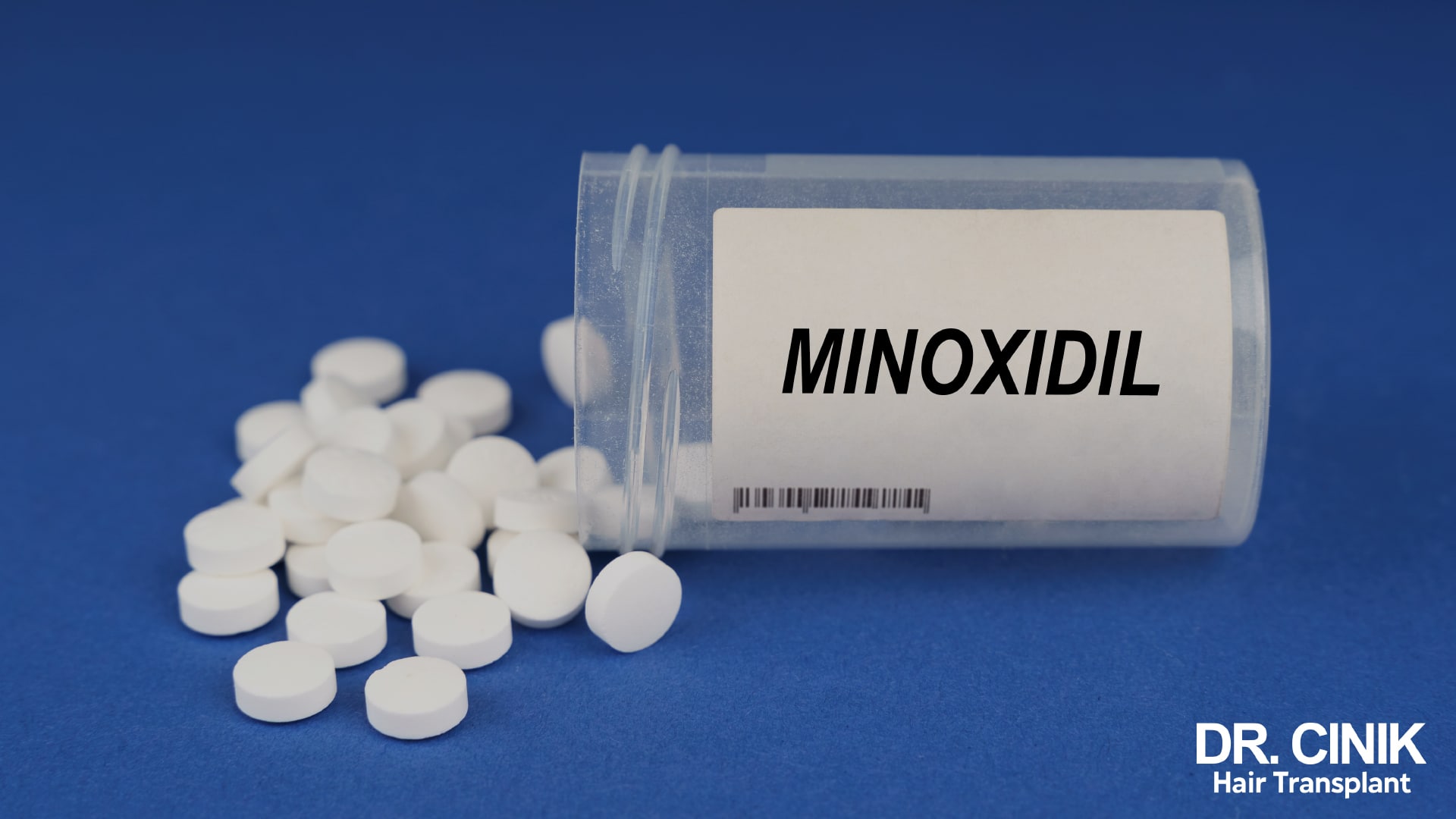 Overturned bottle labelled minoxidil, spilling white tablets onto a blue background