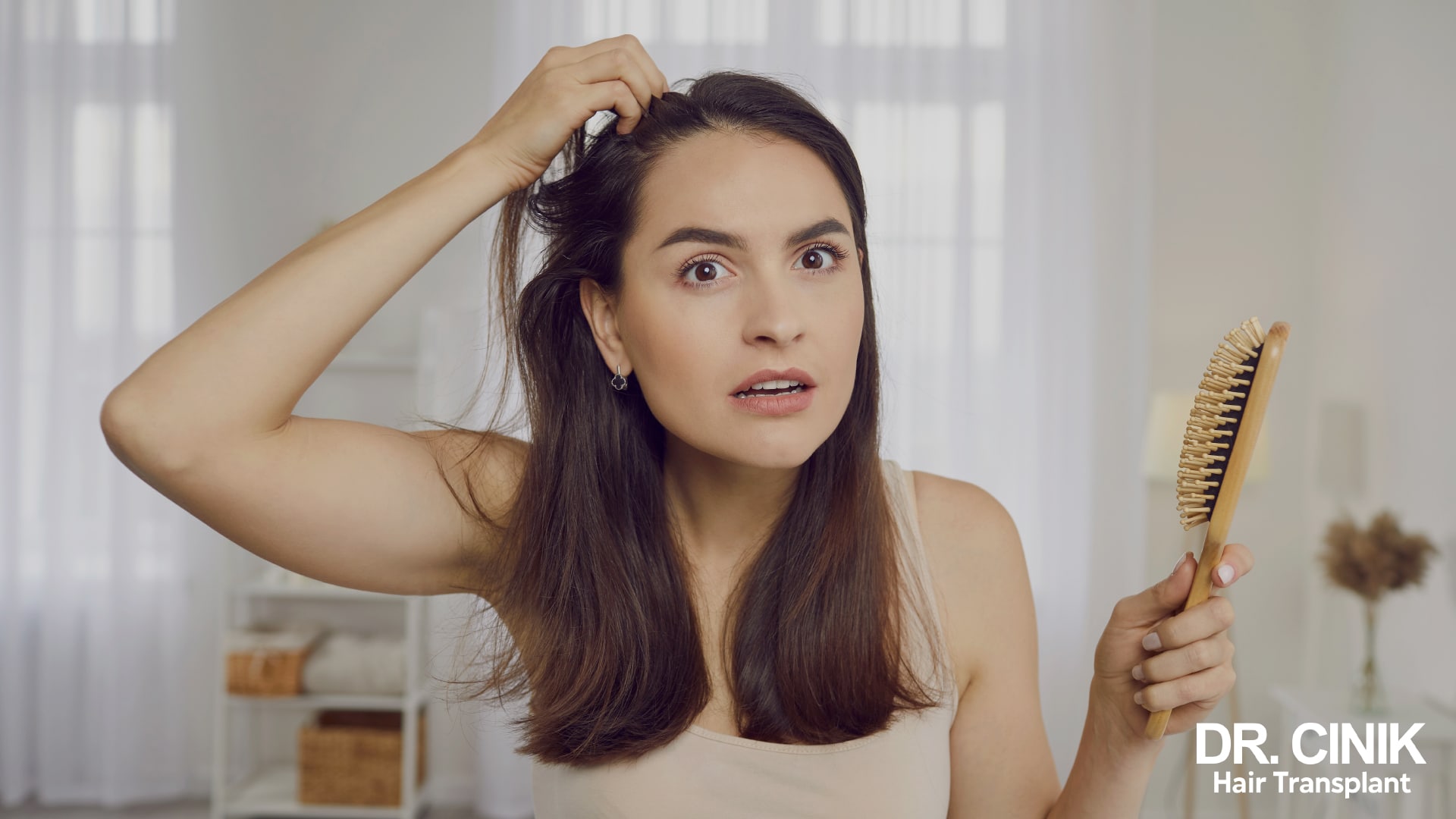 Dark haired woman examining her scalp in front of a mirror, hairbrush in hand