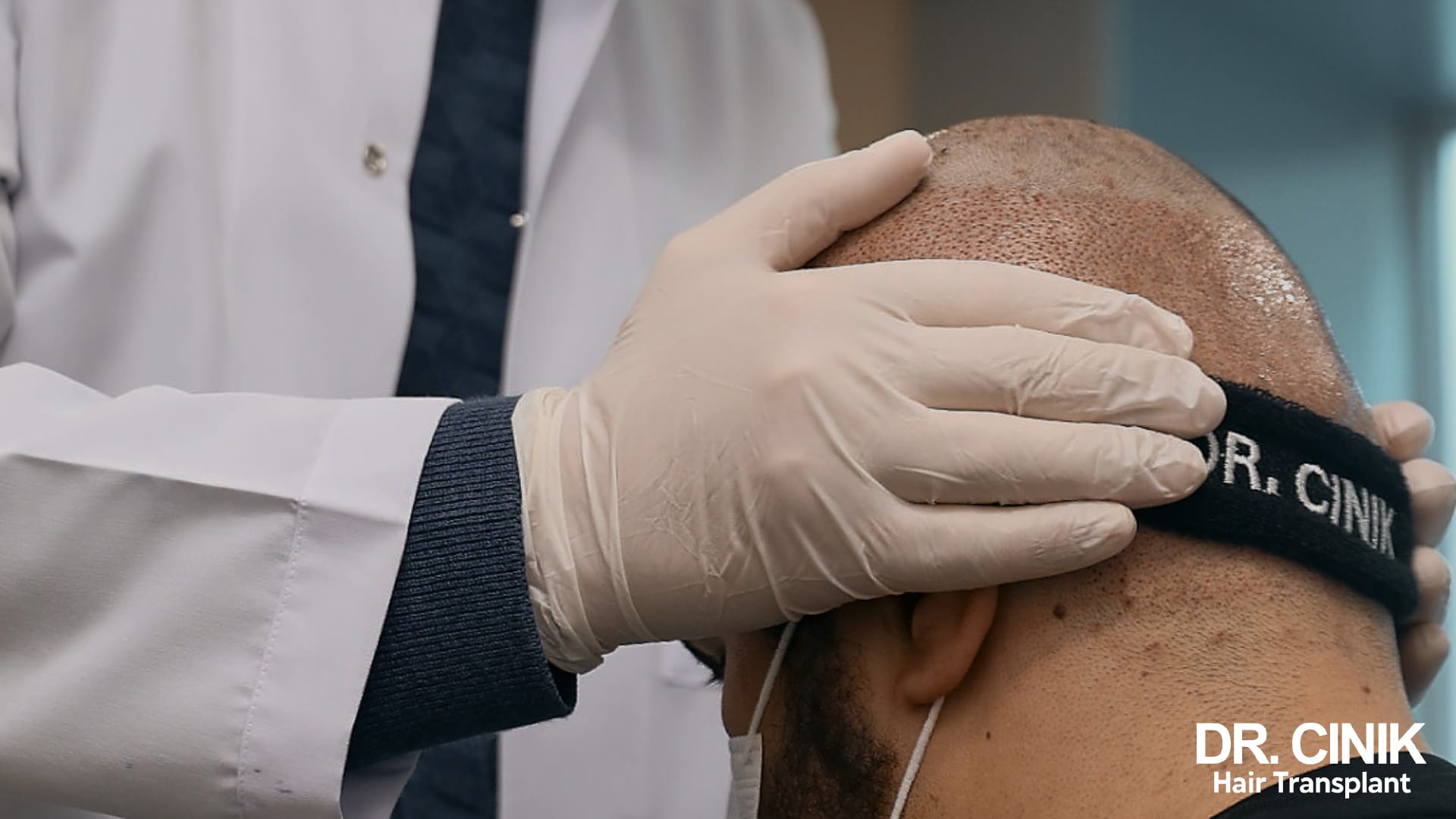 Gloved hand of a doctor adjusting a black compression headband marked Dr Cinik on the forehead of a patient after surgery