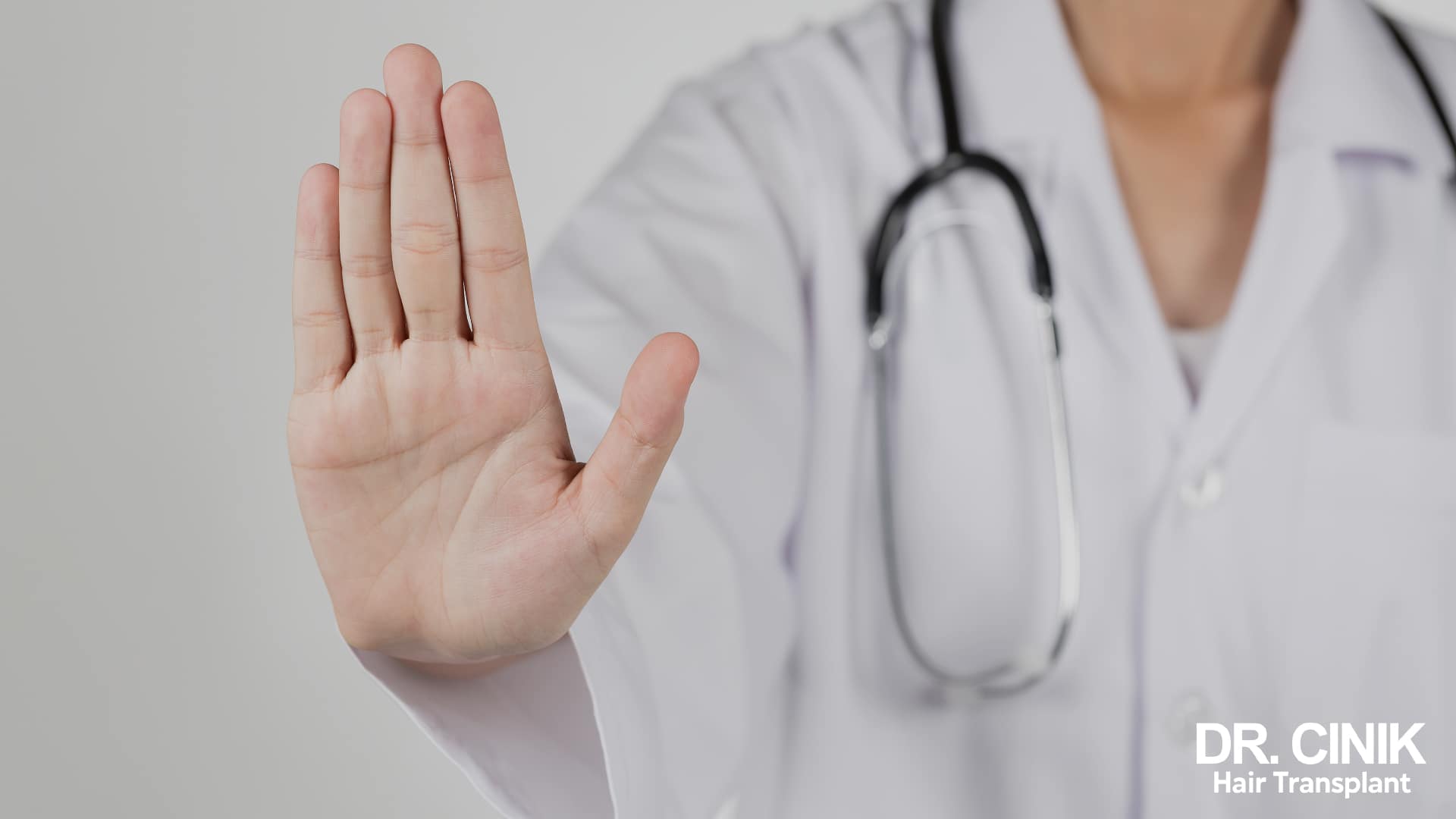 Doctor in a white coat with a stethoscope raising the palm of his hand in a stop gesture