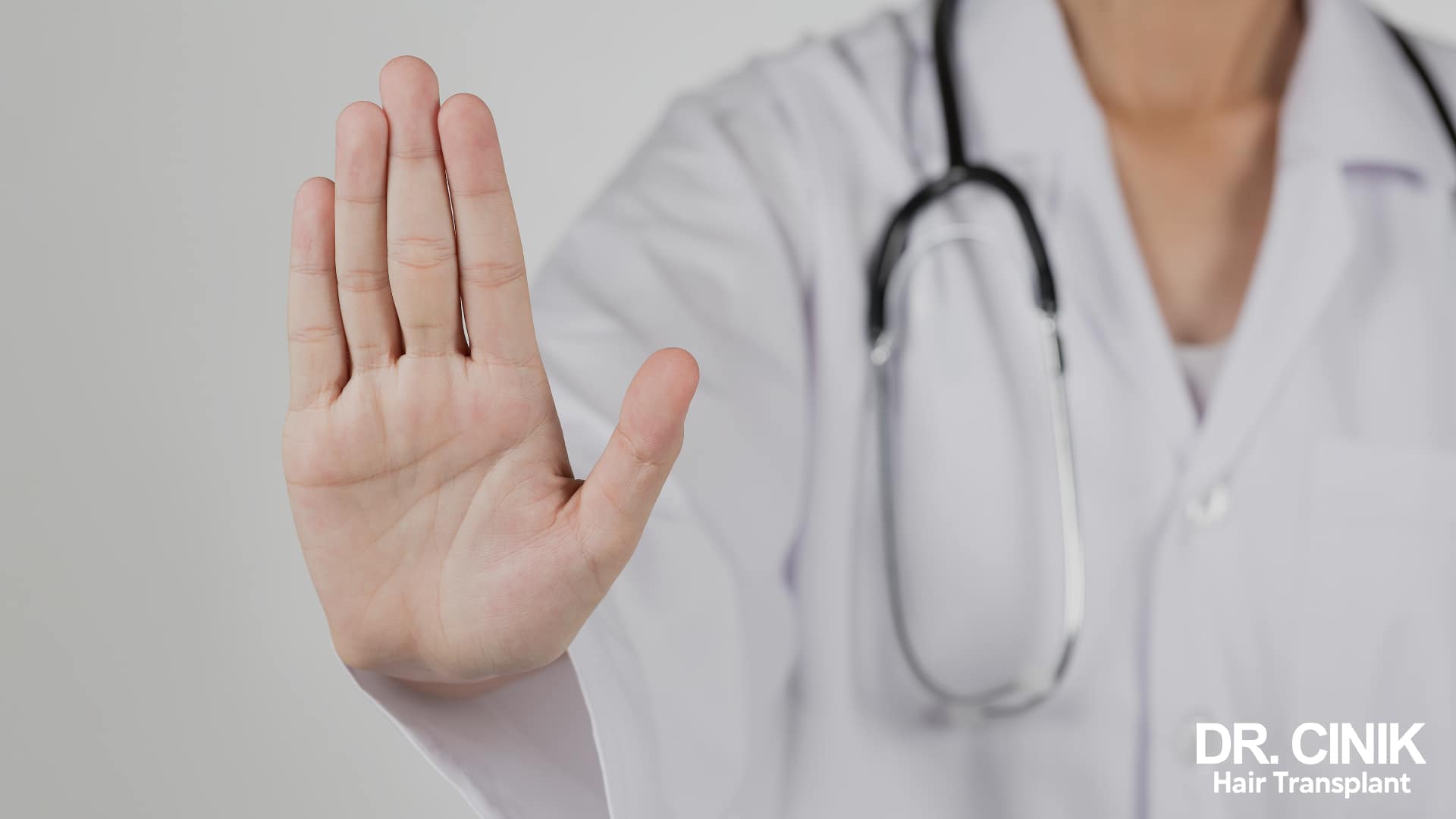 Healthcare worker in a white coat with a stethoscope, palm raised in a stop gesture