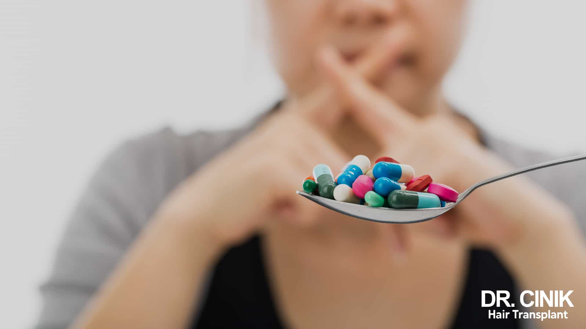 Spoon filled with capsules and tablets of every colour held out in front of a blurred person
