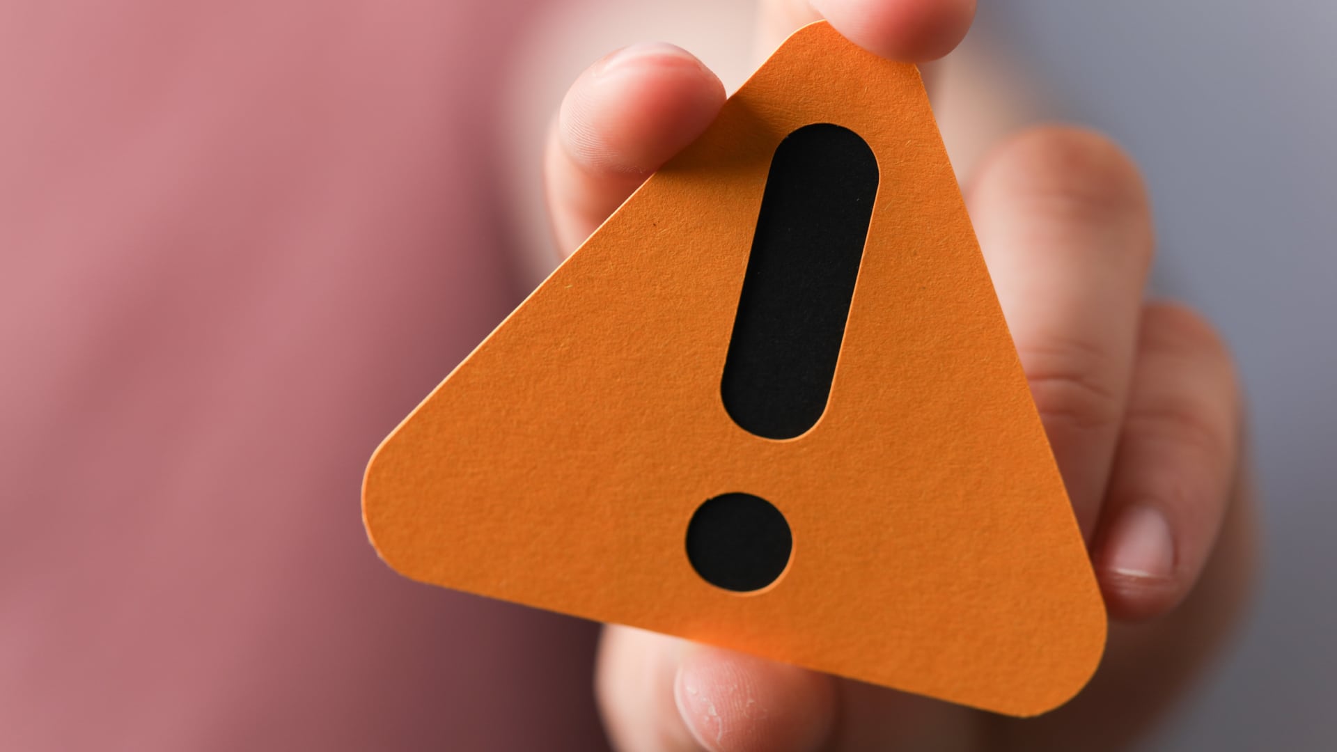 Hand holding an orange triangular sign marked with an exclamation point, as a note of caution