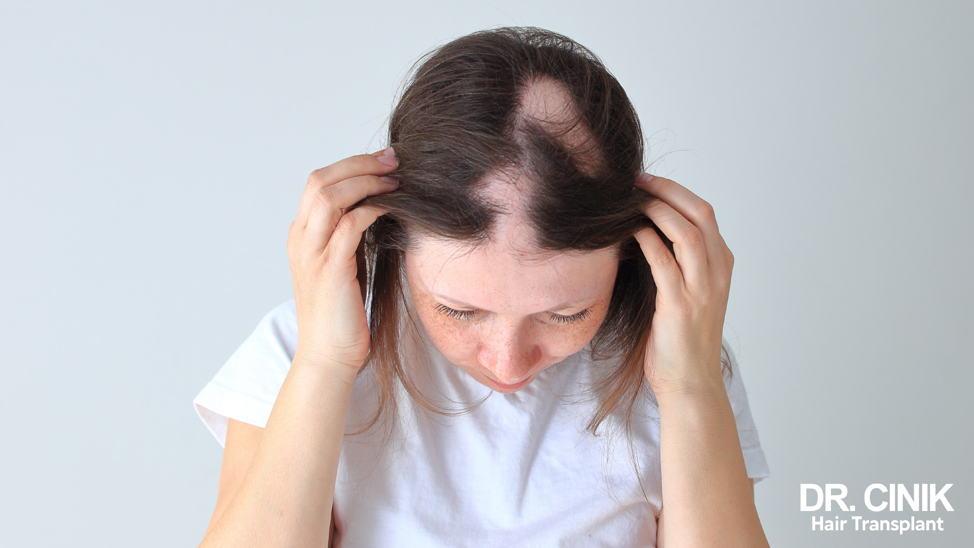 Woman leaning forward and parting her hair over a thinning area on the top of her head