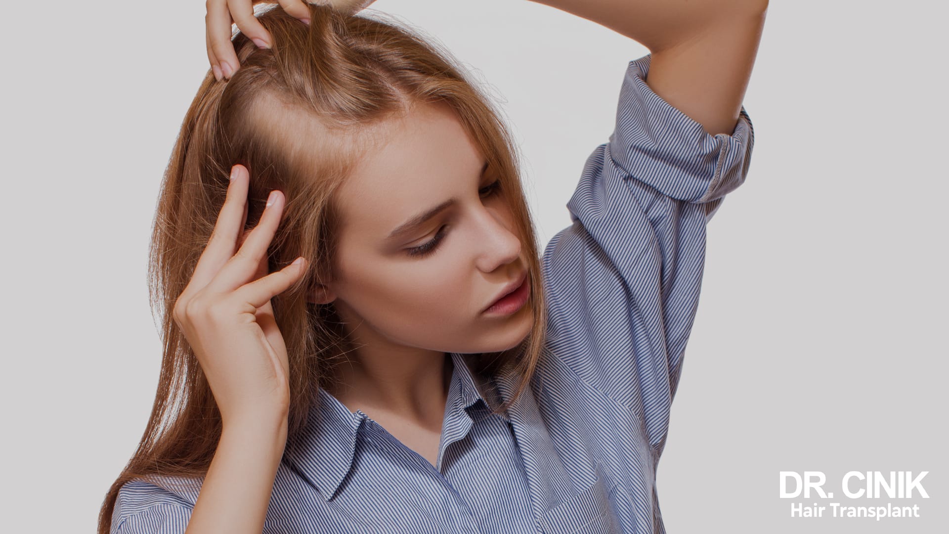 Blonde young woman lifting her hair back: her centre parting has widened and the scalp shows through on top of the head