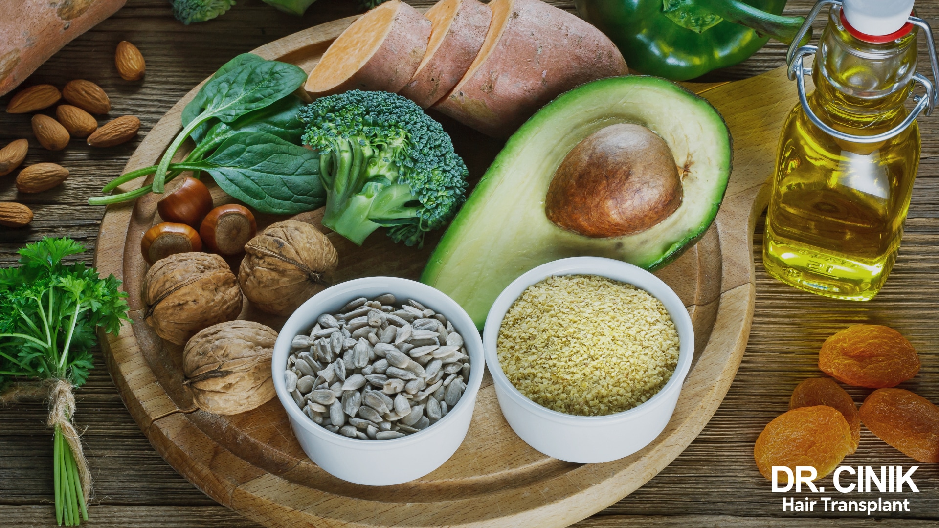 Wooden board laid out with spinach, broccoli, avocado, sweet potato, almonds, walnuts, sunflower seeds and vegetable oil