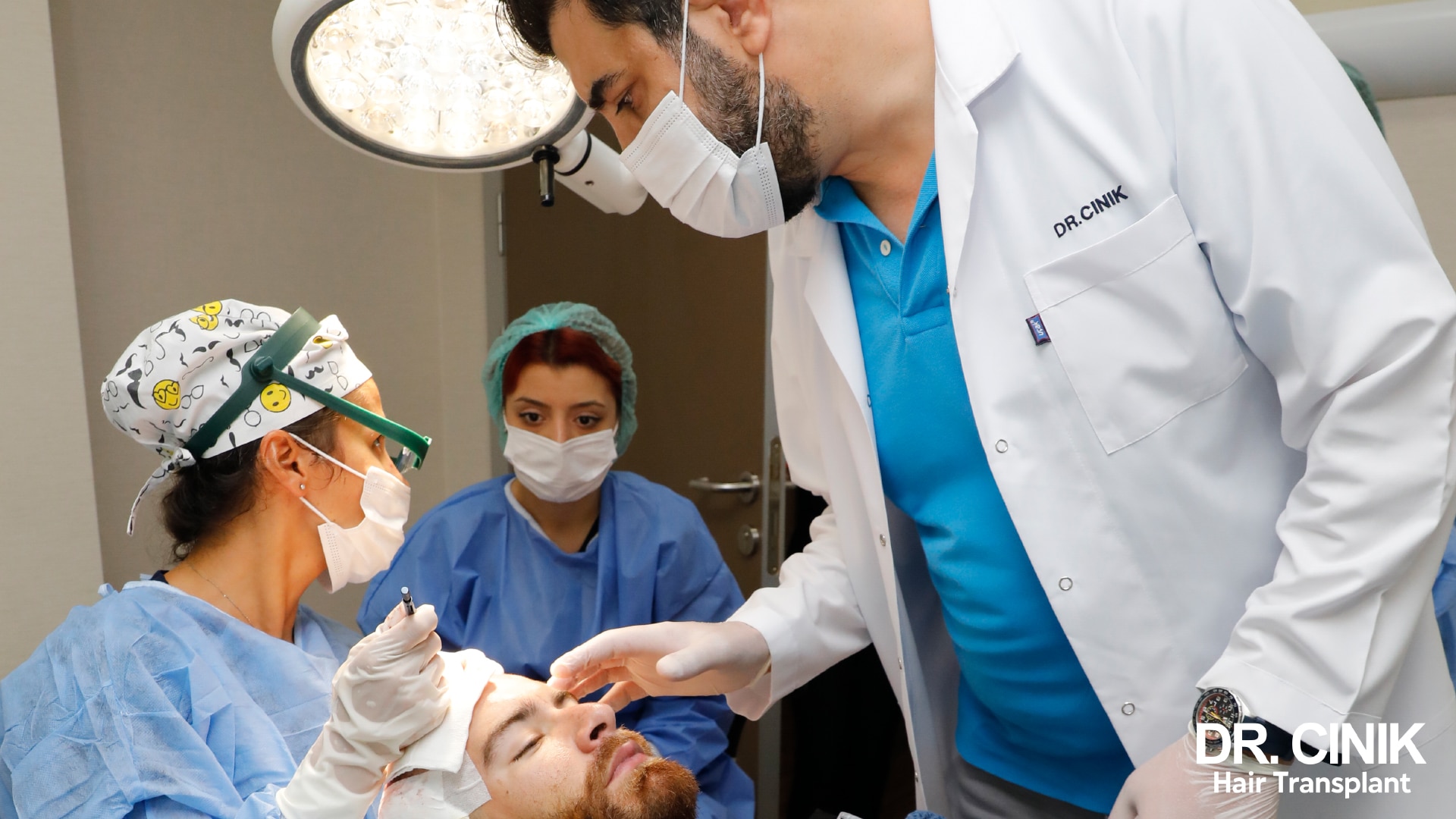 In the operating room, Dr Cinik and two masked nurses lean over a patient to examine his frontal hairline under the surgical lamp