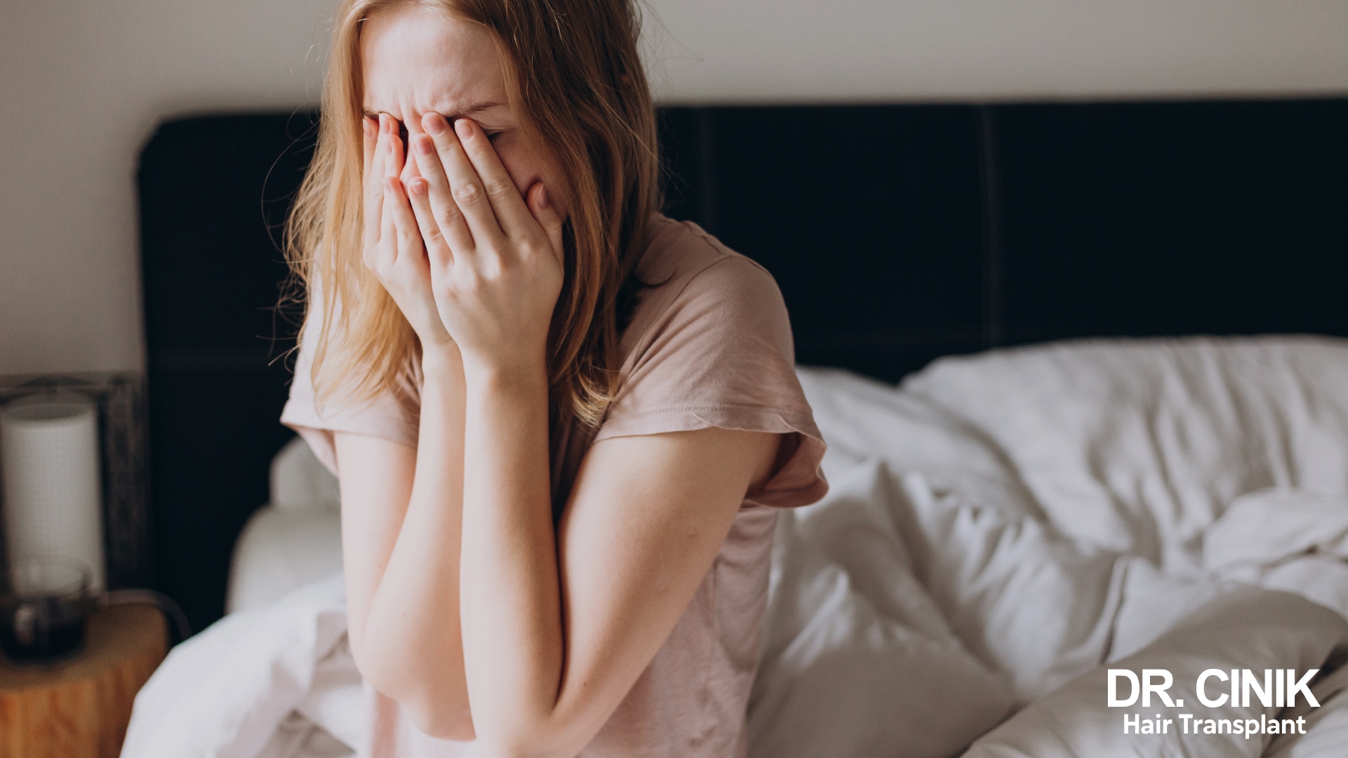 Woman sitting on the edge of her bed on waking, face buried in her hands, exhausted