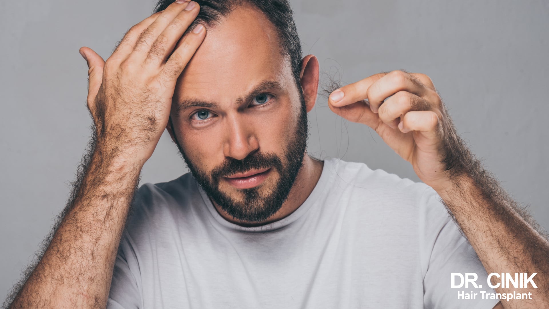 Bearded man looking at a lock of shed hair held between his fingers