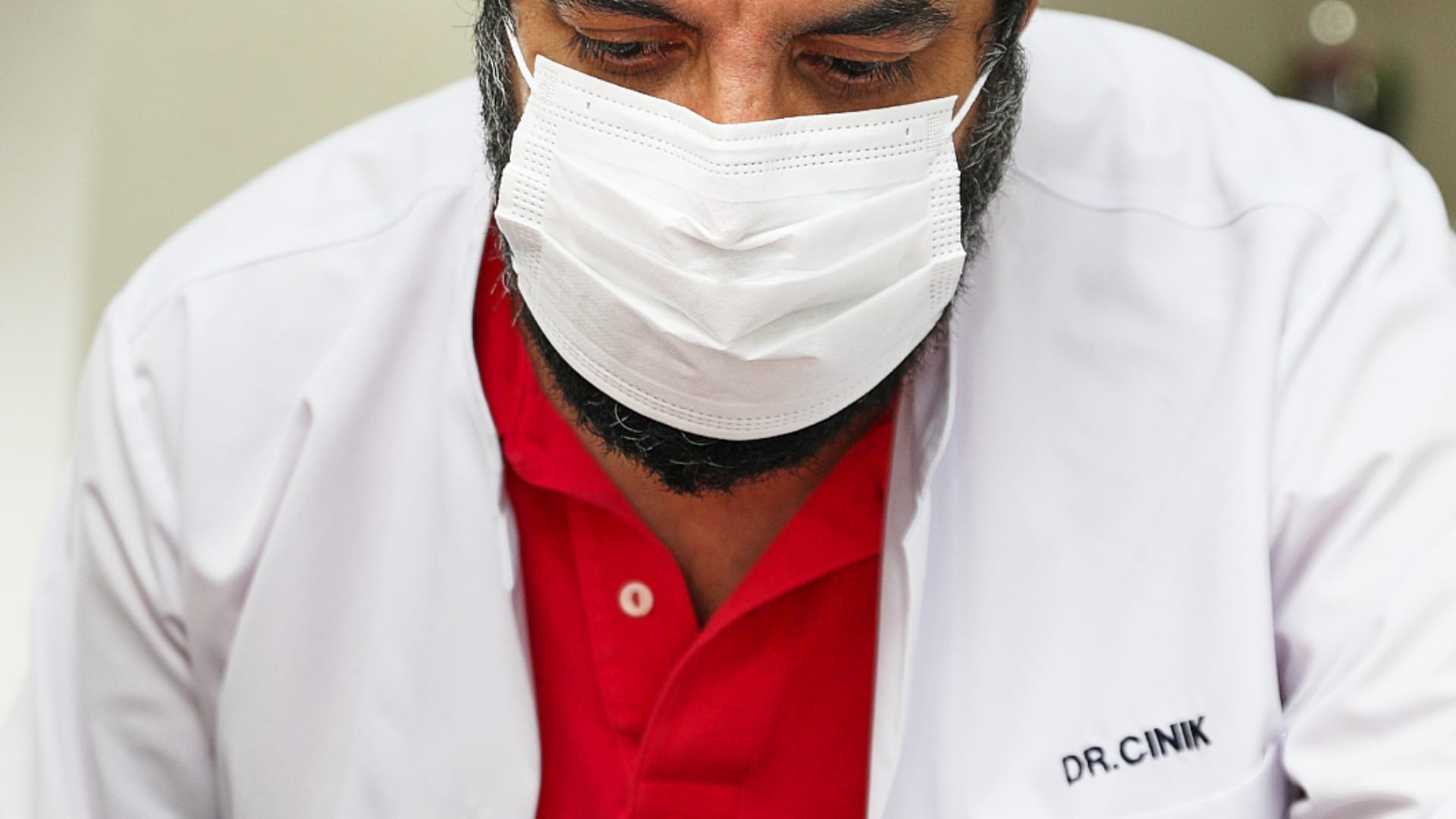 Doctor Emrah Cinik in a white coat and surgical mask, leaning in and focused on his examination