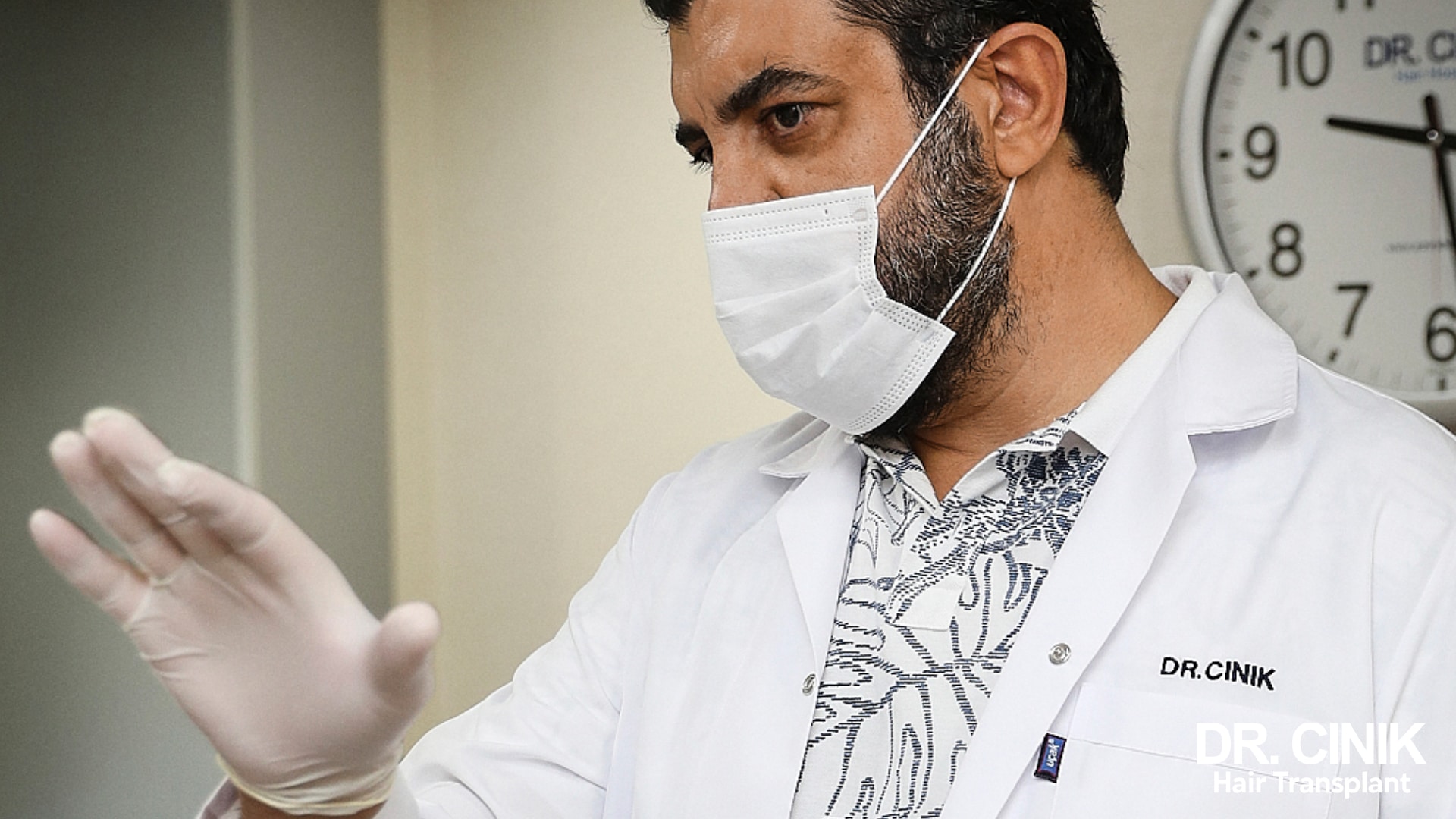 Dr Emrah Cinik in a white coat and surgical mask, gloved, in the middle of an explanation