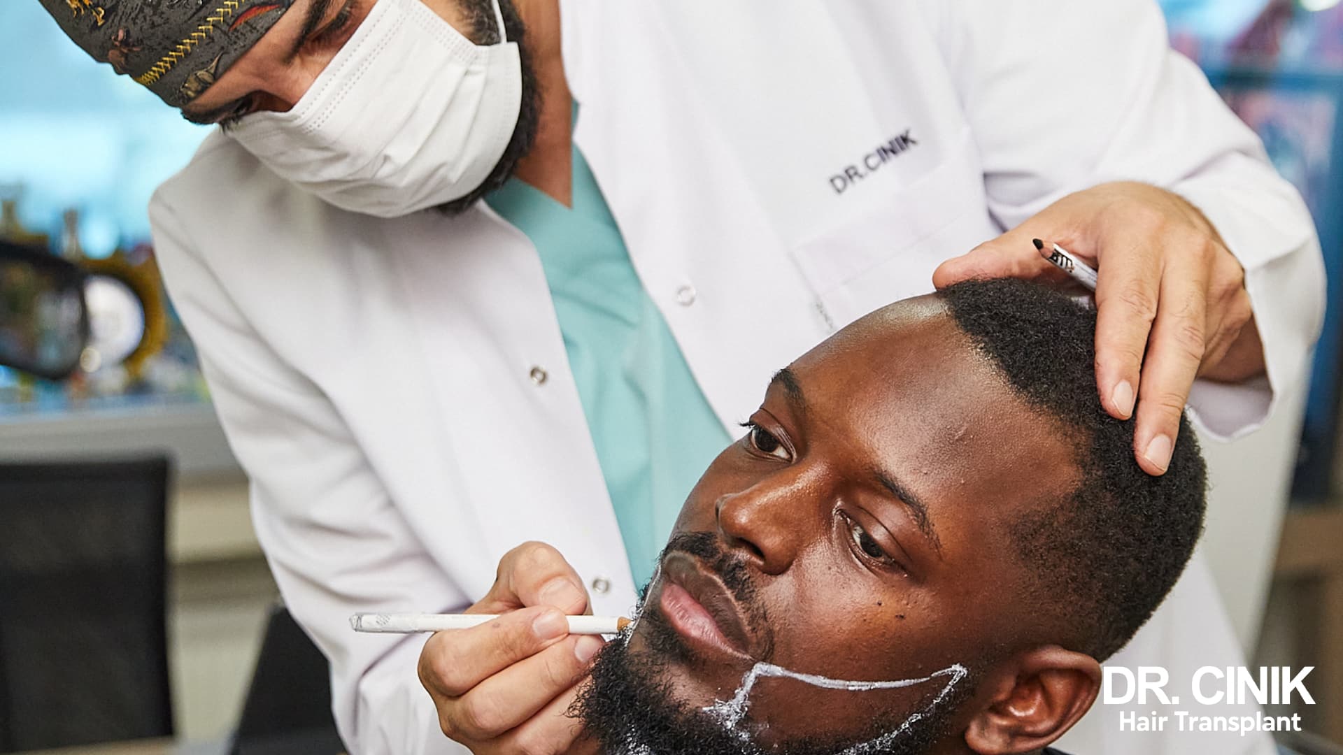 Un praticien en blouse Dr Cinik trace au crayon blanc la future ligne de barbe d'un patient assis