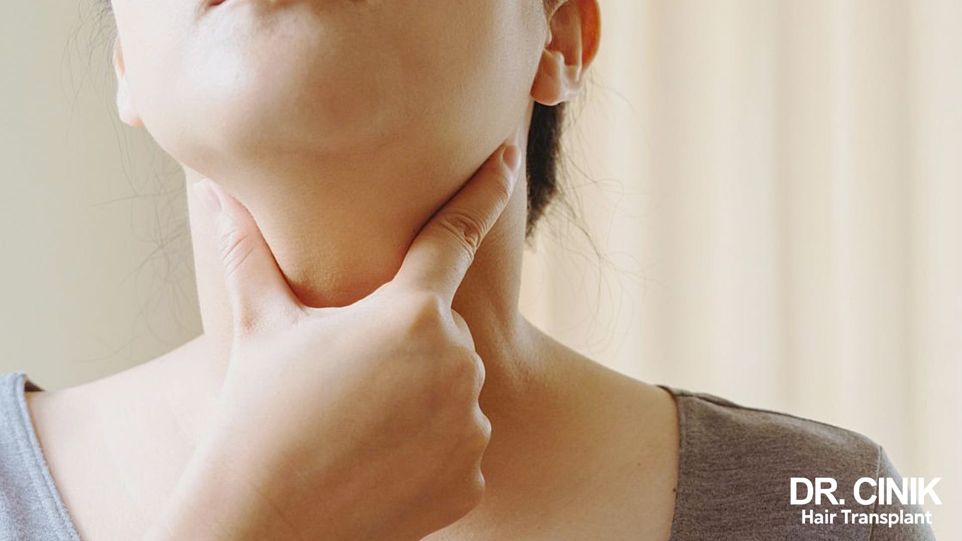Close-up of a woman placing two fingers at the base of her neck, where the thyroid sits