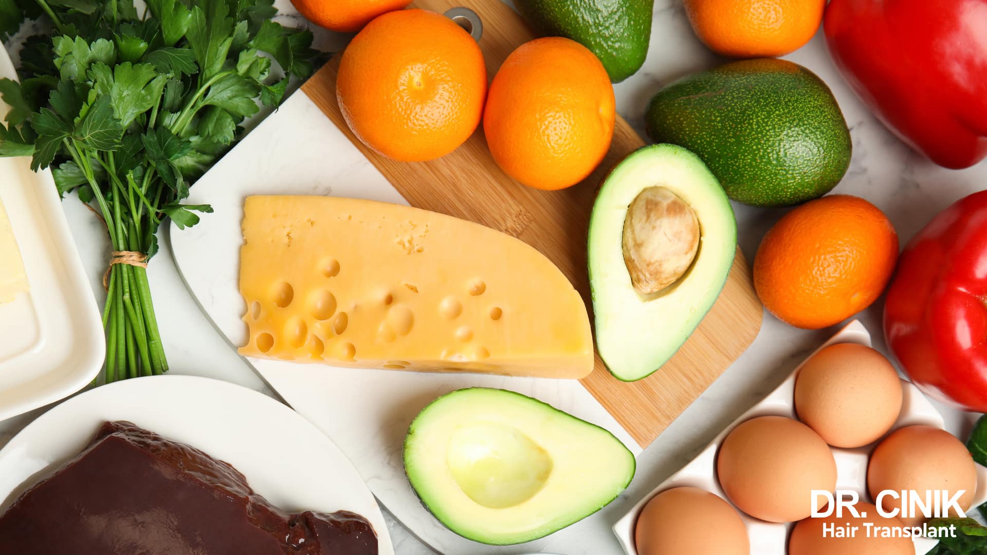 Overhead view of nutrient-rich foods laid out on a board, with citrus fruit, avocados, peppers, eggs, cheese, liver and parsley