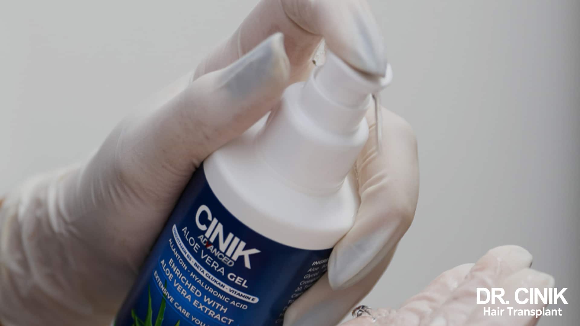Main gantée tenant un flacon pompe de gel de soin post-opératoire à l'aloe vera de la gamme Cinik